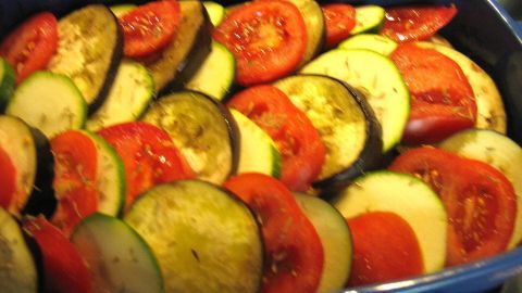 Ein geschichteter Auflauf mit Auberginen und Zucchini in einer blauen Auflaufform, frisch vorbereitet und bereit zum Backen.