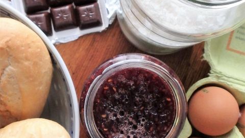 Schokolade, Eier und Marmelade liegen auf einem Holzbrett, bereit für die Zubereitung eines leckeren Schoko-Himbeer-Nachtischs.