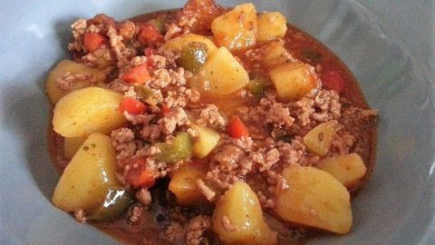 Ein bunter Bauerntopf mit Kartoffeln, Hackfleisch und Gemüse wird in einer blauen Schüssel serviert, appetitlich angerichtet.