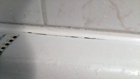 Risse zeigen sich an der Silikonfuge rund um die Badewanne, die feucht und beschädigt aussieht.