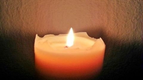 Magische Kerzen sind sehr gut geeignet, um sogar auch bei Wind, ein Lagerfeuer erfolgreich anzuzünden. Eine orangefarbene Kerze brennt sanft in einem dunklen Raum, erzeugt eine warme Atmosphäre für das Lagerfeuer.