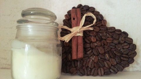 Eine Glasdose mit einer weißen Creme steht neben einem herzförmigen Dekor aus Kaffeebohnen und Zimtstangen.