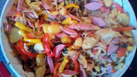 In einer Pfanne braten bunte Kartoffeln mit buntem Gemüse und Würstchen, um eine köstliche Gemüsepfanne zuzubereiten.
