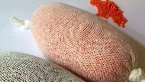 Zwei Kühlpacks aus Linsen liegen nebeneinander, eines rosa und eines grau, in einem hellen Raum.