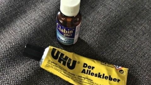 Eine Flasche Clabin und eine Tube Uhu liegen auf einem grauen Stoff untereinander, bereit für die Behandlung von Dornwarzen.