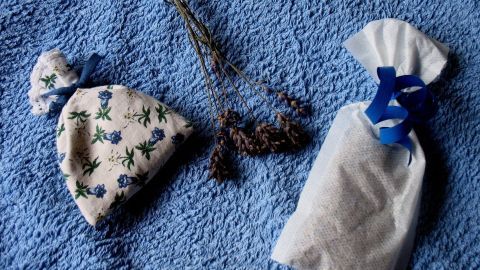 Ein Duftsäckchen liegt auf einem blauen Tuch, umgeben von getrockneten Kräutern, die zum Aromatisieren dienen.
