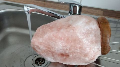Eine große Salzkristall-Lampe wird unter fließendem Wasser im Spülbecken gereinigt, um den Staub zu entfernen.