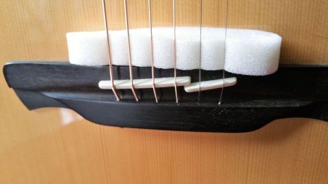 Eine Gitarre zeigt Dämpfungselemente auf dem Steg, um leiser zu üben. Die Saiten sind sichtbar gespannt.