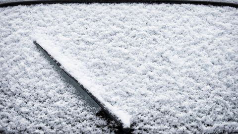 Eine Wischerdüse liegt auf einer mit Schnee bedeckten Windschutzscheibe, die vor Frost geschützt werden muss.