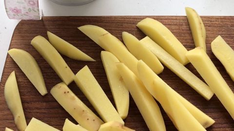 Auf einem Holzbrett liegen frisch geschnittene "schlanke" Pommes, während im Hintergrund eine Topfpflanze steht.