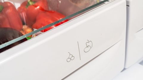 Im Kühlschrank sind frische Paprika sichtbar, während eine Schublade mit Symbolen für Gemüse und Obst geöffnet ist.