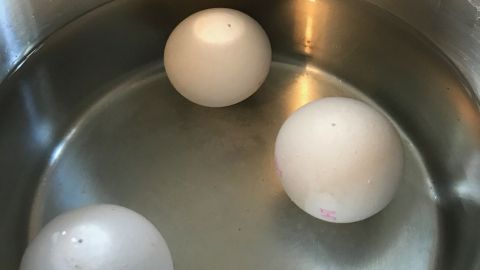 Drei weiße Eier schwimmen in einem Topf mit Wasser auf dem Herd, bereit zum Kochen. Wo ist die Luftblase?