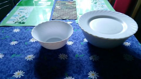 Eine große und eine kleinere weiße Schüssel stehen nebeneinander auf einem blauen Tisch mit Blumenmuster.