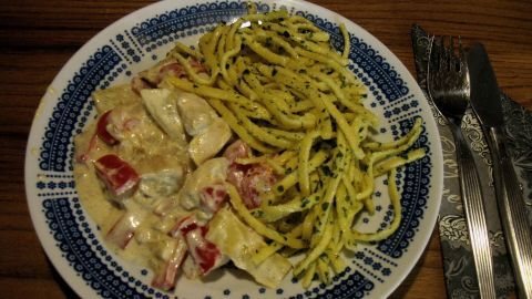 Ein Teller mit Hähnchen-Paprika und Butterspätzle, angerichtet auf einem blau-weißen Geschirr, liegt auf einem Holztisch.
