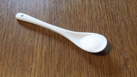 Traubenzucker hilft nicht nur gegen Übelkeit, sondern auch bei Schüttelfrost und es stärkt die Konzentrationsfähigkeit. Ein kleiner, weißer Löffel liegt auf einer Holzoberfläche, bereit, Traubenzucker zur Bekämpfung von Übelkeit zu geben.