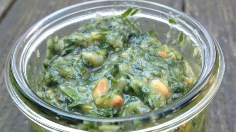 Ein Glas mit grünem Pesto aus Möhrengrün steht auf einem Holzuntergrund, bereit zum Servieren oder Verzehren.