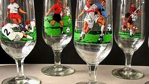 Fünf Weingläser stehen in einer Reihe, jedes mit einem Fußballspieler in Aktion auf einem grünen Feld verziert.
