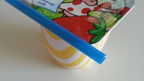 Ein offener Joghurtbecher wird mit einem blauen Strohhalm verschlossen, um den Inhalt zu schützen.