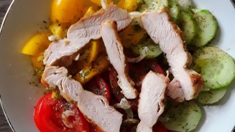 Ein Teller mit gesunden Zutaten wie Tomaten, Gurken und Hähnchenbruststreifen, frisch zubereitet und appetitlich angerichtet.