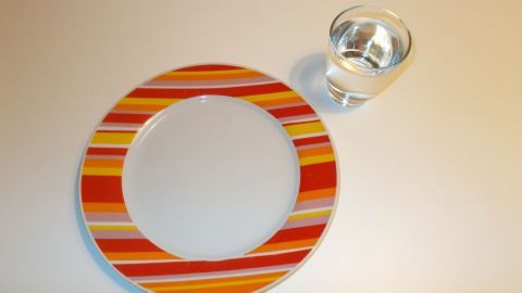 Ein bunter Teller steht leer neben einem Glas Wasser, Symbol für das Prinzip des Intervallfastens zur Gewichtsreduktion.