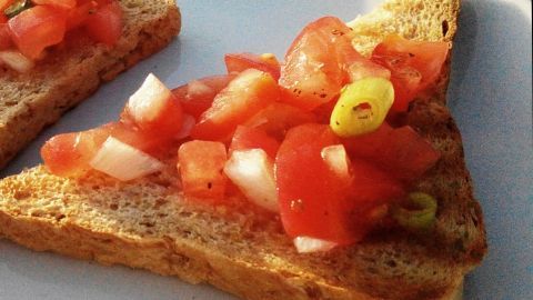 Gebackenes Brot liegt auf einem Teller, belegt mit frischen Tomaten und Zwiebeln, perfekt für eine Bruschetta.