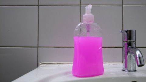 Ein leerer Seifenspender steht auf dem Waschbecken und enthält eine pinke Flüssigkeit, daneben ist ein Wasserhahn.
