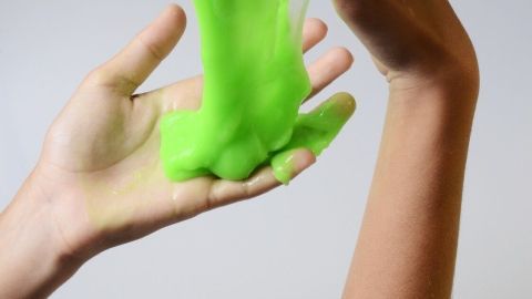 Helle grüne Knetmasse wird von zwei Händen gedehnt, während sie in einem neutralen Hintergrund leicht schimmert.