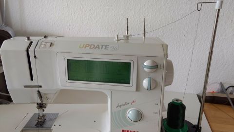 Eine Nähmaschine mit Garnrollenhalter, der waagerecht positioniert ist, steht auf einem Tisch in einem hellen Raum.