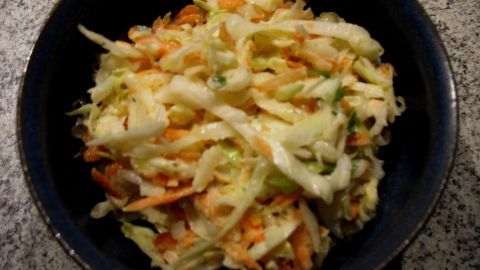 Ein bunter Spitzkohl-Apfel-Karotten-Salat liegt in einer schwarzen Schüssel auf einer marmorierten Oberfläche.