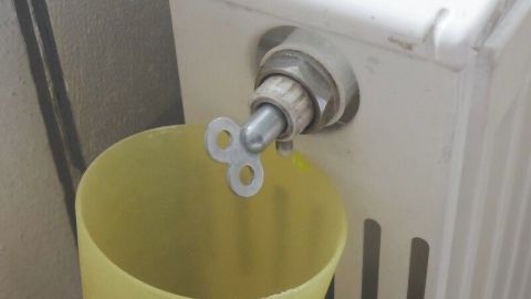 Ein Heizkörper mit einem Entlüftungsventil, aus dem Luft entweicht, während ein gelber Eimer darunter steht.