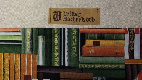 Ein Bücherregal aus verschiedenen bunten Bücher in antikem Stil. Oben ist ein Label mit mittelalterlicher Schrift, das "Würzburger Bücherkorb" zeigt.