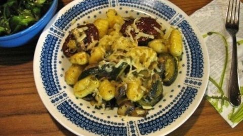 Eine bunte Gemüsepfanne mit Gnocchi liegt genussvoll auf einem dekorativen Teller, umgeben von einem Salat in einer Schüssel.