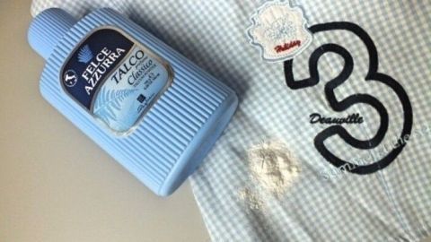 Ein Flasche mit Fleckenentferner liegt auf einem karierten Hemd, das einen Speiseöl-Fleck zeigt.