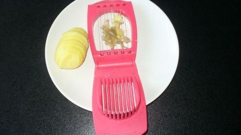 Pellkartoffeln liegen neben einem pinken Schneider, der zum gleichzeitigen Schneiden und Schälen verwendet wird.