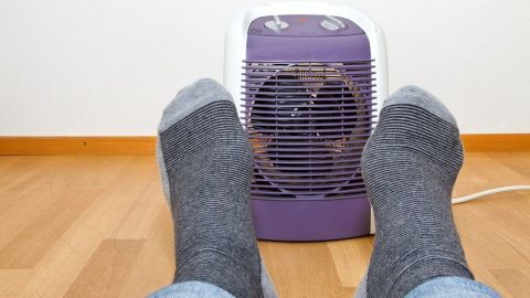 Graue Socken liegen vor einem Heizlüfter, der warme Luft ausstößt, um kalte Füße in einem Innenraum zu wärmen.