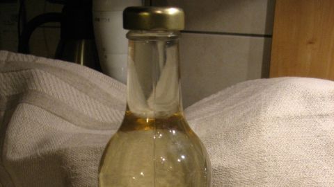 Eine klare Glasflasche steht auf einer Arbeitsfläche und enthält Hefewasser, umgeben von einer neutralen Unterlage.