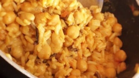Ein Topf mit Kichererbsen-Curry wird mit einem blauen Löffel umgerührt, um die Aromen zu vermischen.