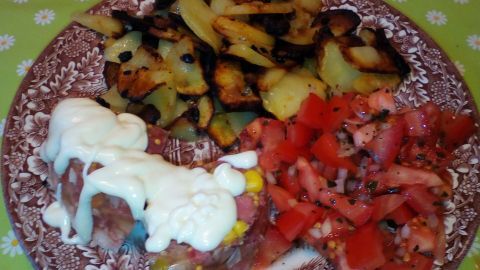 Ein Teller mit Bratkartoffeln, umgeben von Sülze und frischem Salat, an einem hellen Tisch serviert.