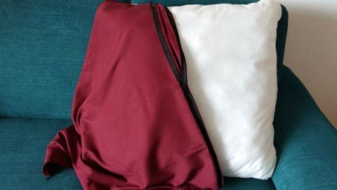 Eine Kissenhülle in Rot verdeckt teilweise ein weißes Kissen auf einer blauen Couch, die gemütlich wirkt.