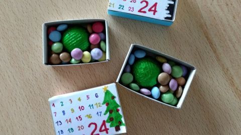 Mini-Adventskalender aus Streichholzschachteln mit bunten Süßigkeiten und einem grünen Ball im Inneren, auf einem Tisch.