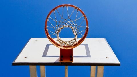 Ein Basketballkorb hängt hoch über dem Boden, der klare Himmel im Hintergrund vermittelt ein Gefühl von Weite und Freiheit.