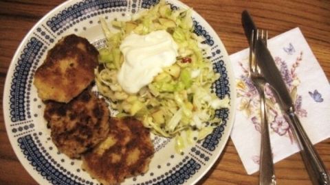 Kartoffelrösti liegen neben frischem Spitzkohlsalat auf einem Teller, garniert mit einer Portion Sahne, auf einem Holztisch.