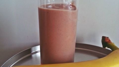 Ein frisch zubereiteter Bananen-Kokos-Smoothie steht in einem Glas auf einem silbernen Tablett, daneben eine Banane.