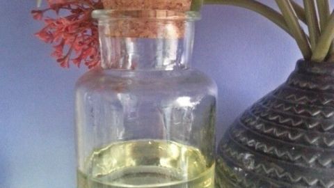 Ein Glas Öl steht auf einem Regal, umgeben von Blumen. Es vermittelt eine gepflegte Hautpflege-Atmosphäre.