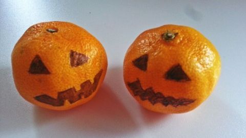 Zwei orangefarbene Mandarinen sind geschnitzt und sehen aus wie gruselige Kürbisse, perfekt für Halloween-Dekoration.