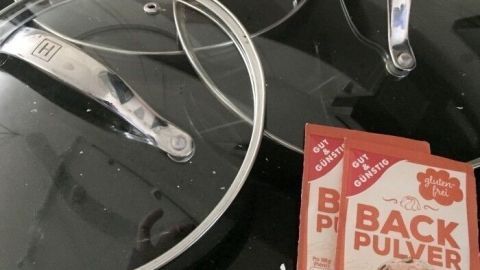 Drei Glasdeckel liegen auf einer dunklen Oberfläche, während Backpulver daneben bereitgestellt wird.