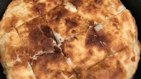 Ein rundes, goldbraunes Pite Tetovar liegt in einer Pfanne, gleichmäßig in Stücke geschnitten, bereit zum Servieren.