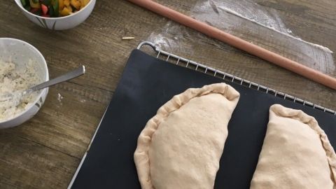 Zwei rohe Calzone-Teigstücke liegen auf einer Arbeitsfläche, umgeben von frischem Gemüse und Füllungen für Pizza Calzone türkischer Style.