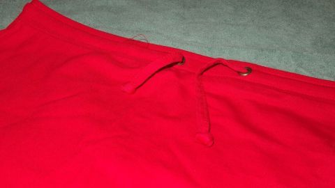 Rote Kleidung liegt auf einem grauen Untergrund, zeigt die Schnur und ist frisch gewaschen, ohne Anzeichen von Ausbleichen.