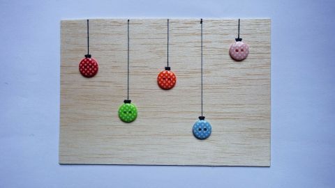 Eine Balsaholz-Postkarte zeigt fünf farbige hängende Ornamente auf einem einfarbigen Hintergrund, geeignet für DIY-Projekte.